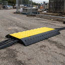 Yellow and black three channel cable protector ramp laid across a site access road with cables running through it