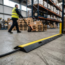 Black and yellow single channel rubber cable cover protecting a power cable across a warehouse walkway as a pallet truck crosses