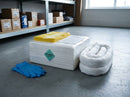 White oil and fuel absorbent pads and coiled white socks from a 120 litre spill kit refill pack on a workshop floor, with yellow disposal bags, cable ties and blue nitrile gloves, parts shelving behind
