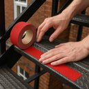 Person applying red anti-slip tape to fire escape stair step edge — safety installation