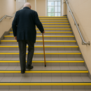 High-visibility yellow anti-slip stair nosing on UK public building staircase - DDA accessible step edge safety for elderly person