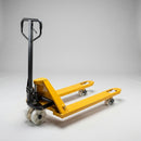 2500kg manual hand pallet truck on a plain grey studio background showing the yellow steel forks, black hydraulic pump and tiller handle and white nylon steering wheels