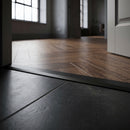 Black anodised 26mm aluminium T-bar threshold strip fitted between matt black porcelain tiles and dark walnut herringbone flooring