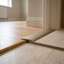 Champagne anodised 26mm aluminium T-bar threshold strip fitted between stone-effect tiles and natural oak laminate in a UK bedroom doorway