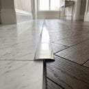 Electro Polished 26mm aluminium T-bar threshold strip fitted flush between white marble tiles and dark oak herringbone parquet