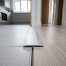 Silver 26mm aluminium T-bar threshold strip fitted between grey porcelain tiles and pale oak laminate in a UK kitchen doorway