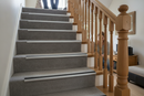 Heavy duty carpet stair nosing with grey insert installed on UK home carpeted staircase - man and woman using stairs safely