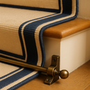 Antique brass stair rods fitted on carpeted stair step with cream and navy bordered runner — period British home