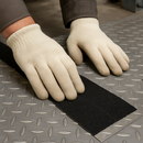 Person applying conformable anti-slip tape to diamond plate metal surface — foil backing pressing into pattern