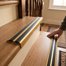 Gold anodised 36mm slim aluminium stair nosing with twin black rubber inserts being fitted to oak laminate stairs in a UK home