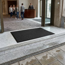 Black ribbed polypropylene entrance mat on marble hotel lobby floor with people walking toward reception