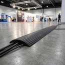 Black cable protector in use on an exhibition hall floor with power cables running through its channels