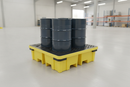 Four steel 205-litre drums stored on a yellow polyethylene 4 drum spill containment pallet with black mesh grille deck and forklift access pockets, shown in a warehouse