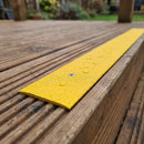 Close-up of the fine grit surface of a yellow 50mm GRP decking strip screwed flat to a deck board