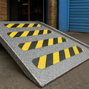 Black and yellow conformable tape on raised checker plate ramp surface — hazard marking on uneven metal