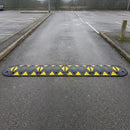 Black rubber speed bump with yellow reflective triangles bolted in a single run across the entrance lane of a commercial car park