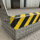 Black/yellow conformable anti-slip tape on metal stair nosing edge — bends over step profile