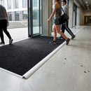 Professional entrance mat with white PVC trim beading creating smooth floor transition in modern building lobby