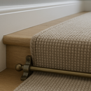 Close-up of bronze stair rod with ball finial securing a beige carpet runner on an oak step
