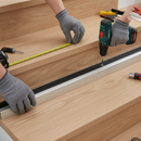 Person installing aluminium stair nosing on wooden step using cordless drill screw-fix method