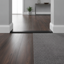 Black PVC floor transition strip installed in modern UK hallway between dark laminate and charcoal carpet