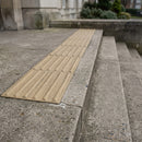 Beige corduroy hazard warning tactile paving bonded across a concrete landing at the top of external steps