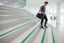 Anti-slip bullnose stair nosing with Green insert — installed on UK staircase, semi-rounded profile with person using stairs