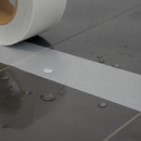 Close-up of clear anti-slip tape on tile surface — subtle grit texture visible when light catches it