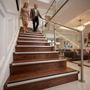 A couple walks up a modern wooden staircase with stainless steel handrails in a bright, upscale home interior.