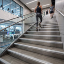 A woman in athletic wear runs up a wide indoor staircase, with other people visible further up the stairs in a modern building interior.