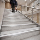 Modern interior staircase with light gray speckled steps and brushed metal rails, with two people walking up the stairs in a bright office or lobby.