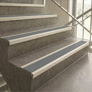 Gray non-slip rubber stair strips installed on concrete stairs with white metal rails and a glass railing.