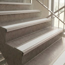 White metal stair tread strips installed on concrete stairs next to a glass window.