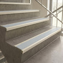 Light gray non-slip stair tread strips installed on concrete stairs next to a glass railing.