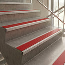 Red and silver metal stair tread protectors installed on a concrete staircase next to a glass railing.