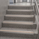 A set of indoor stairs with speckled gray concrete steps and light beige non-slip rubber strips, shown alongside a stainless steel handrail.