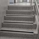 A set of modern indoor stairs with textured gray concrete steps, silver metal handrails, and black rubber anti-slip strips on each step.