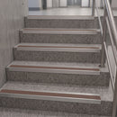A set of modern stainless steel handrails installed along a terrazzo-patterned staircase with integrated light wood hand grips.