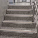 A set of modern stainless steel stair nosing strips installed on gray speckled terrazzo stairs, with a metal handrail on the right.