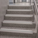 Gray terrazzo stair treads with white non-slip strips installed on an indoor staircase with a metal railing.
