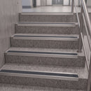 A set of modern stainless steel step rails installed on gray speckled terrazzo stairs, shown with a metal handrail on the right.