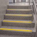 Concrete stairs with bright yellow non-slip rubber steps and a stainless steel handrail in a modern indoor hallway.