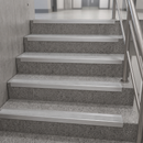 A set of modern stainless steel handrails installed along a terrazzo-patterned staircase with integrated metal grab bars.