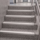 White metal stair nosing strips installed on gray speckled terrazzo stairs with a stainless steel handrail.