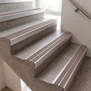 Close-up of an indoor staircase with textured gray stone steps and metallic silver metal stair nosings and handrail.