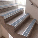Staircase steps with textured gray non-slip strips on the risers and treads, installed in a residential interior with a wall and metal handrail visible.
