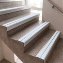 White metal stair nosing and handrail trim installed on outdoor concrete steps with a stone-tile finish, next to a beige wall and a metal handrail.