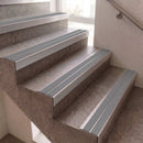 Light gray stair step strips installed on a set of concrete stairs with a metal handrail nearby.