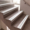 White metal stair nosing strips installed on gray stone steps in an indoor staircase.