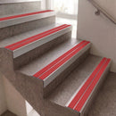 Red and silver stair grips installed on concrete stairs in an indoor setting.